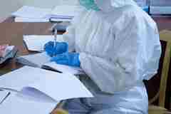 A healthcare professional writing notes in protective clothes