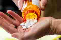 An image of prescription medication in a jar being poured into a hand. 