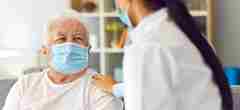 An elderly patient with a healthcare professional wearing masks and talking. 